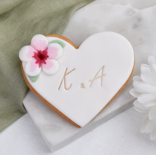 Ciasteczko z białym lukrem w kształcie serca z dużym, ozdobnym kwiatkiem.