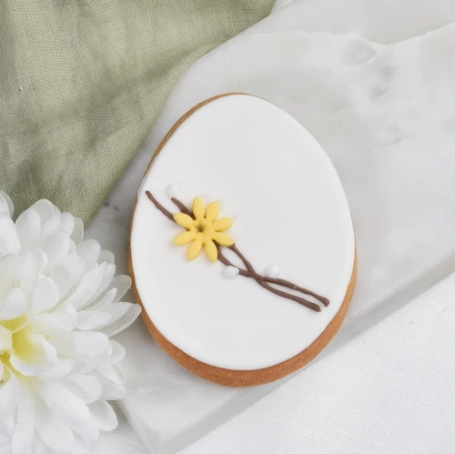 Ciasteczko lukrowane w kształcie pisanki, zdobione motywem wiosennych gałązek bazi i kwiatkami.