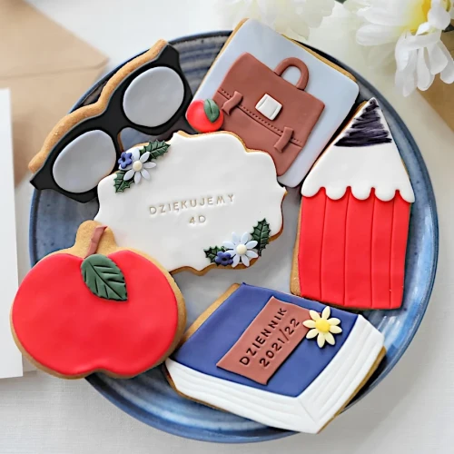 Ciasteczka lukrowane z motywami szkolnymi: okulary, kredka, dziennik szkolny i kwiaty.