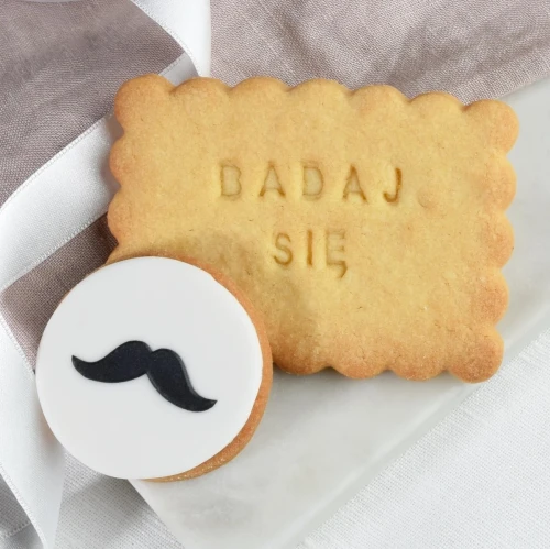 Zestaw ciasteczek: maślane ciasteczko z napisem i lukrowane ciasteczko z wąsami.