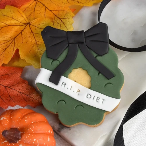 Ciasteczka lukrowane na Halloween w kształcie wieńca z czarną wstęgą.