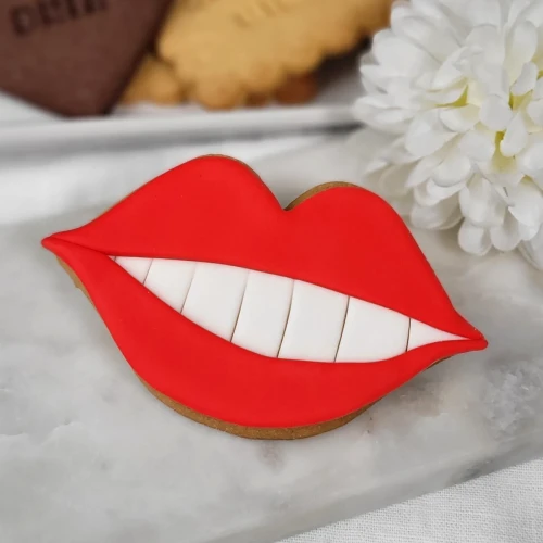 Ciasteczko maślane w kształcie ust ze śnieżnobiałym uśmiechem.